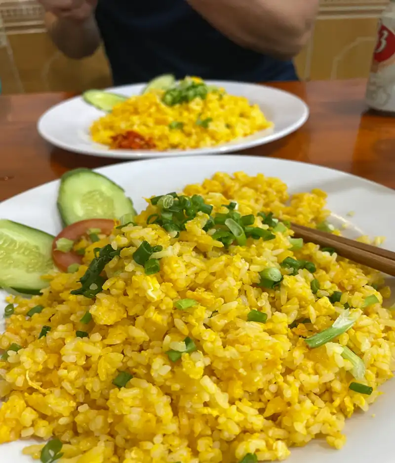 Gelber gebratener Reis auf einem weißem Teller mit braunen Essstäbchen