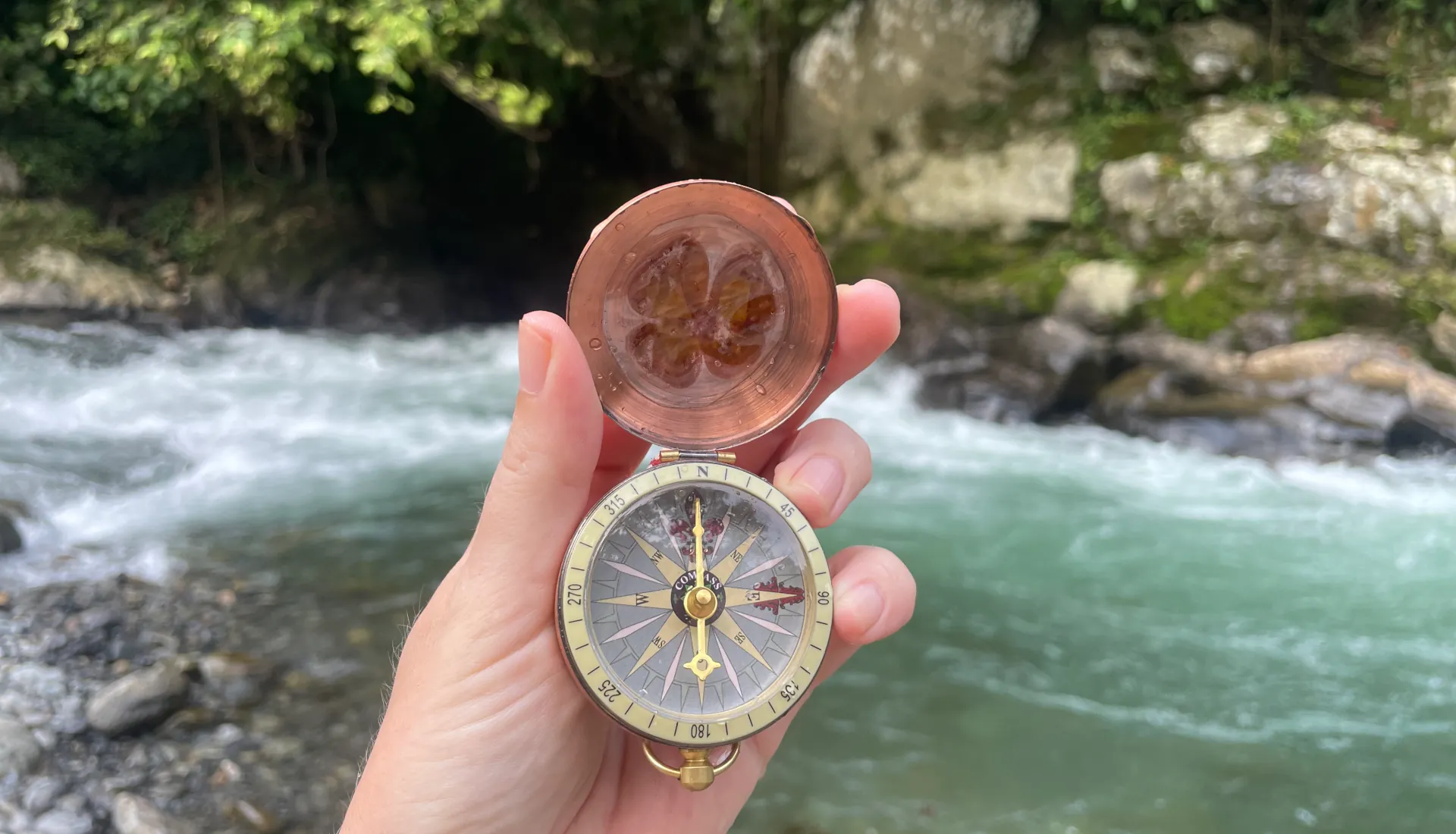 kompass in der hand und im Hintergrund ein Fluss mit blick auf das andere ufer