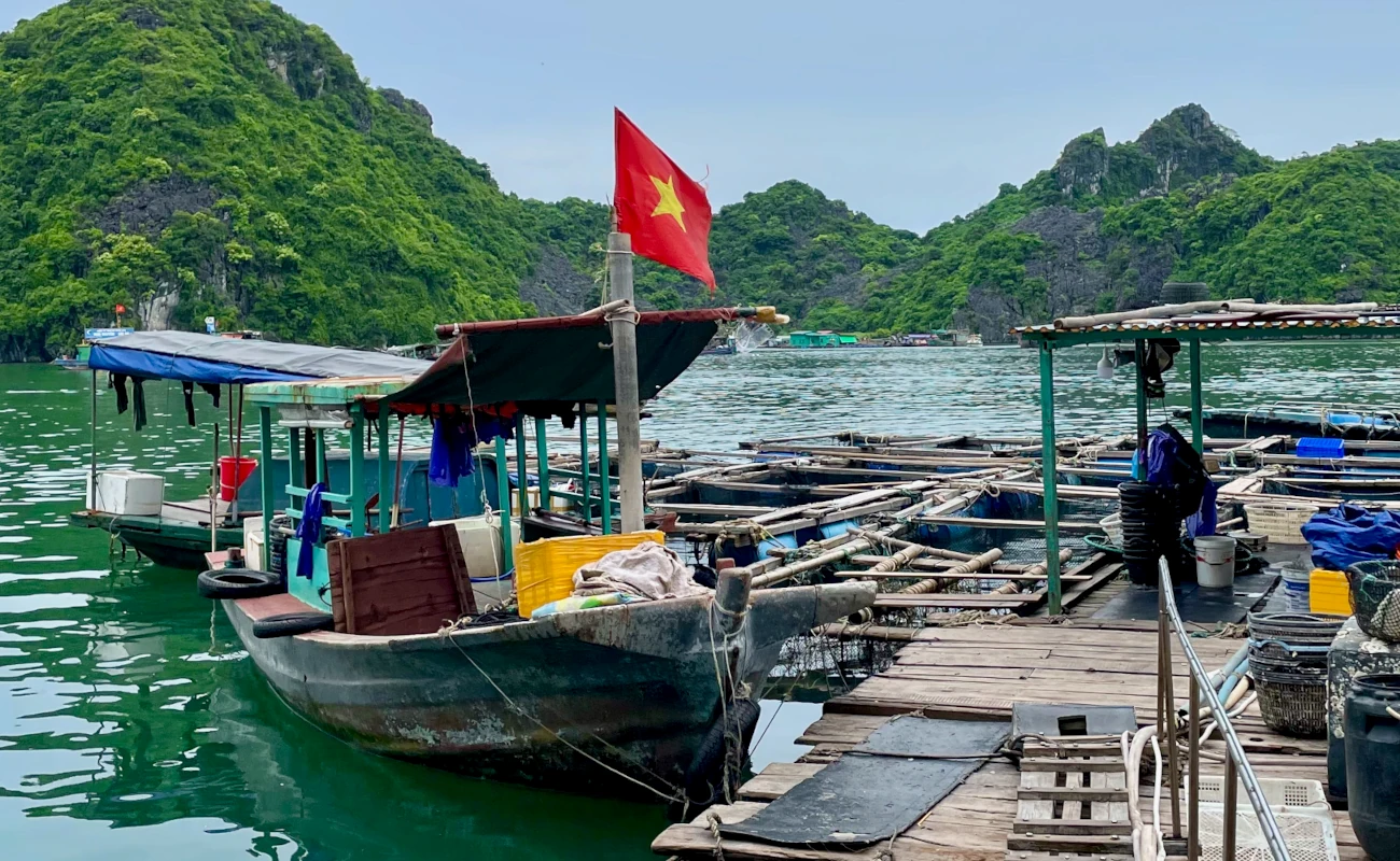 verborgene halongbucht in cat ba. ein fi9scherboot liegt an einem provisorisch gebauten Holzsteg. Gehisst sit die Flagge vietnams und einige plastiktonnen mit fischernetzen stehen auf dem steg.