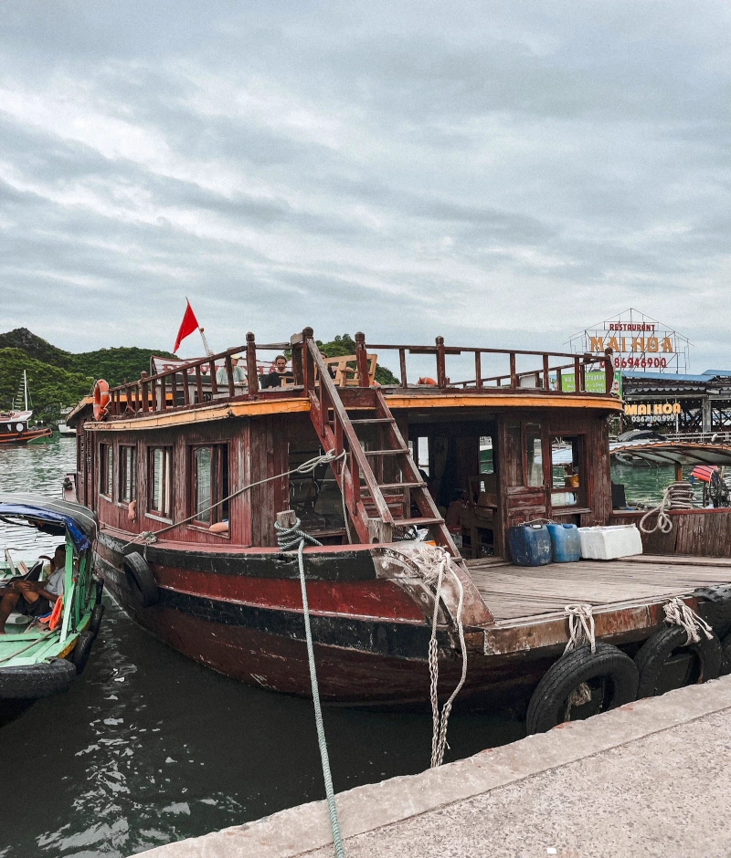 vergorgene halong bucht. ein holzboot liegt im hafen. es wird als fähre genutzt auch wenn es nicht so aussieht. es hängen taue und reifen rings herum am boot.
