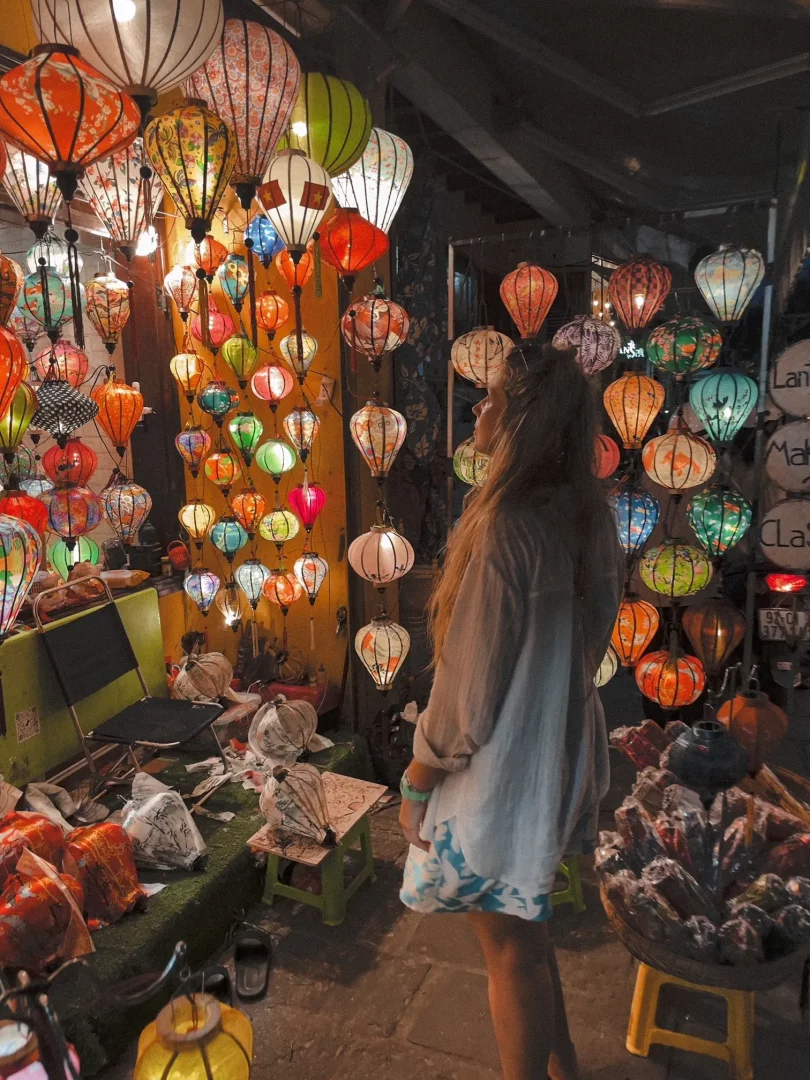 jenno pineapple steht vor einem kleinen straßenstand an dem eine menge bunter kleiner lampions hängen. es ist dunkel und die lampen leuchten in vielen bunten farben